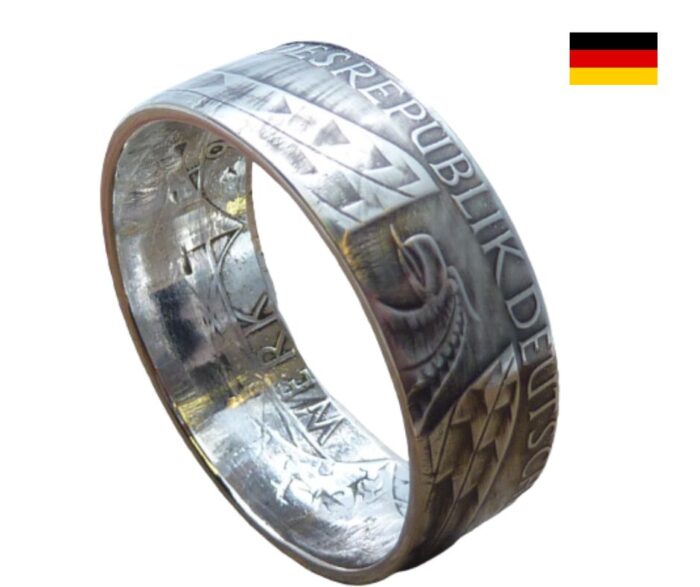 Der Silberring mit dem deutschen Bundesadler ist in der Tat ein bemerkenswertes Schmuckstück, das sowohl durch sein Design als auch durch seine Herkunft besticht. Hier sind einige weitere Aspekte, die möglicherweise für Interessierte von Bedeutung sein könnten: Weitere Merkmale und Vorteile: Einzigartigkeit: Jeder Ring wird aus einer originalen 10 DM Münze gefertigt, was ihn zu einem Unikat macht. Die Gebrauchsspuren oder das Design der Münze verleihen jedem Ring einen individuellen Charakter. Symbolik: Der Bundesadler ist ein starkes Symbol für Deutschland und steht für Freiheit, Stärke und die deutsche Einheit. Träger dieses Rings können sich mit diesen Werten identifizieren. Anpassungsfähigkeit: Der Ring kann sowohl von Männern als auch von Frauen getragen werden und eignet sich dank seiner schlichten Eleganz für verschiedene Anlässe, sei es im Alltag oder zu besonderen Feierlichkeiten. Gravuroption: Die Möglichkeit, einen persönlichen Gravurtext hinzuzufügen, eröffnet viele Verwendungsmöglichkeiten: Sei es als Verlobungsring, Freundschaftsring oder für Jubiläen. Die Gravur sorgt dafür, dass das Schmuckstück zu einem persönlichen Andenken wird. Pflegehinweise: Um die schöne Optik des Rings zu bewahren, sollte er regelmäßig gereinigt werden. Es empfiehlt sich, ihn vor dem Kontakt mit Chemikalien (z. B. beim Baden oder Putzen) abzunehmen. Dieser Ring fasst sowohl ästhetische als auch emotionale Werte zusammen und kann eine lebendige Verbindung zur deutschen Kultur darstellen. Egal ob für sich selbst oder als besonderes Geschenk: der Silberring mit dem Bundesadler ist eine bleibende Erinnerung an eine wichtige Zeit und Geschichte.