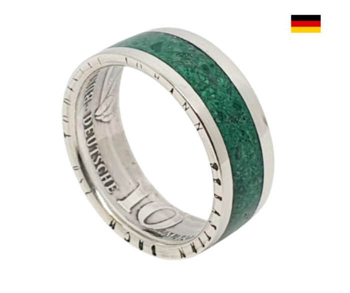 Dieses handgefertigte Schmuckstück ist ein einzigartiger Silberring, der aus einer originalen 10 DM Münze gefertigt wird. Der Ring beeindruckt durch sein edles Design, das durch ein Inlay aus hochwertigem Malachitstein zusätzlich aufgewertet wird. Produktdetails: Materialien: 925er Silber und Malachit Breite: ca. 9,0 mm Stärke: ca. 1,5 mm Individuelle Gravur: Auf Wunsch kann ein persönlicher Text innen im Ring graviert werden. Besonderheiten: Jeder Ring wird mit viel Liebe in unserer kleinen Manufaktur hergestellt und kann an Ihre besonderen Wünsche angepasst werden. Die Verwendung einer echten 10 DM Münze macht jeden Ring zu einem einzigartigen Unikat. Das Inlay aus feinem Malachitstein verleiht dem Ring einen Hauch von Eleganz und Stil. Wichtige Hinweise: Bitte beachten Sie, dass der Ring aus einer Münze gefertigt ist, was bedeutet, dass Unregelmäßigkeiten in Form, Farbe und Jahrgang auftreten können. Das Beispielbild dient lediglich zur Veranschaulichung, und der tatsächliche Ring kann in Details abweichen. Dieser einzigartige Ring ist nicht nur ein Schmuckstück, sondern auch ein bedeutungsvolles Erinnerungsstück, das speziell für Sie hergestellt wird. Ideal als Geschenk oder für den eigenen Schmuckkästchen – zeitlos und individuell!