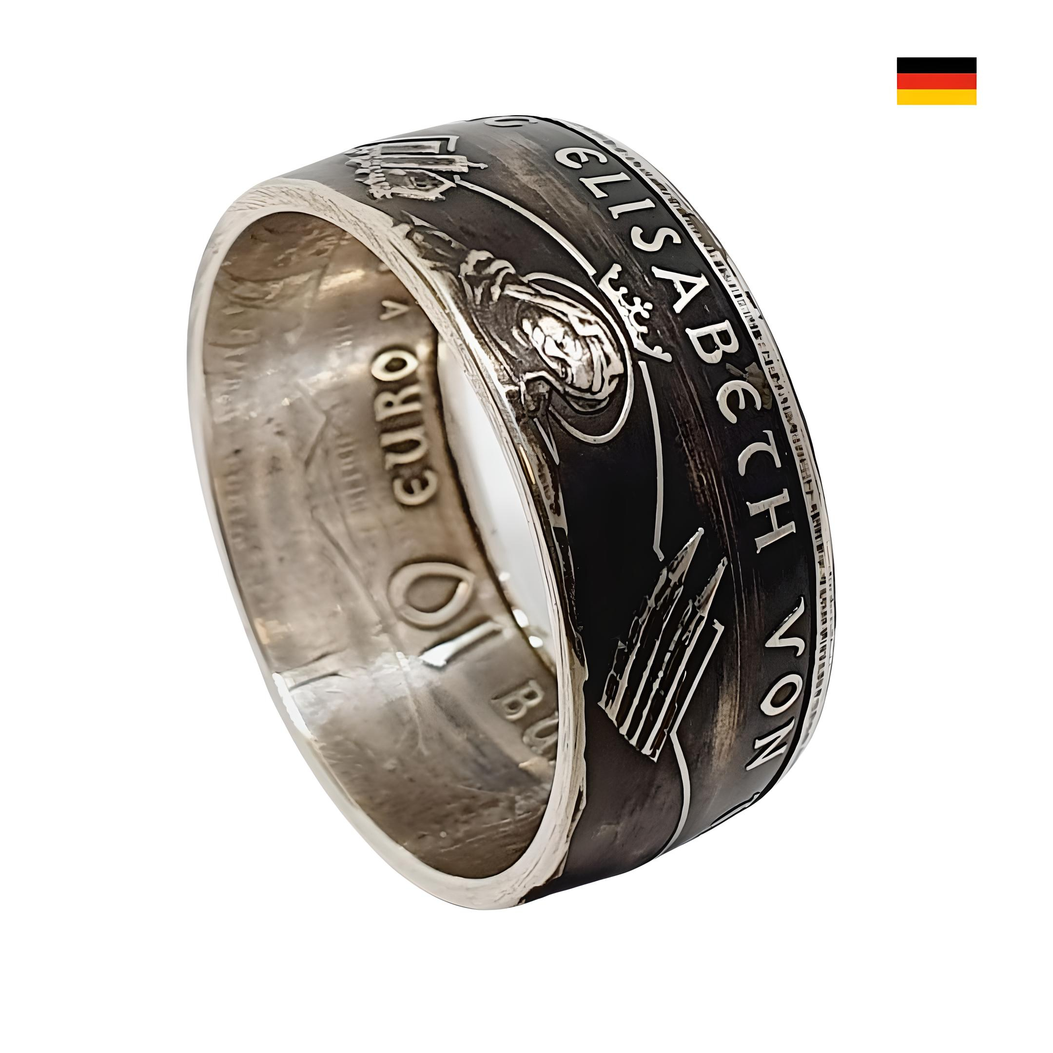 Produktbeschreibung: Münzring aus 10 Euro Münze (Silber 925) Entdecken Sie den einzigartigen Münzring, gefertigt aus einer originalen 10 Euro Münze aus dem Jahr 2007, die die beeindruckende Elisabeth von Thüringen darstellt. Dieser exklusiveRing verbindet historisches Erbe mit modernem Design und ist somit das perfekte Schmuckstück für jede Gelegenheit. Details zum Ring: Original Münze: 10 Euro Münze von 2007 Motiv: Abbildung von Elisabeth von Thüringen mit dem Text "800. GEBURTSTAG ELISABETH VON THÜRINGEN" Randschrift: „WIR SOLLEN DIE MENSCHEN FROH MACHEN“ Material: 925er Silber (Sterlingsilber) Breite: ca. 10 mm Stärke: ca. 2 mm Gravurmöglichkeiten: Um den Ring noch persönlicher zu gestalten, bieten wir Ihnen die Möglichkeit einer Innengravur nach Wunsch. Hier sind einige Beispiele für schöne Gravuren: „Meine Liebe“ „Für immer“ Dieser Münzring ist mehr als nur ein Schmuckstück – er ist ein wunderschönes Erinnerungsstück an die bedeutende Figur der Elisabeth von Thüringen und ihre Botschaft der Nächstenliebe. Bitte beachten Sie, dass die Beispielbilder in Form und Farbe abweichen können. Jedes Stück wird in Handarbeit gefertigt. Machen Sie diesen einzigartigen Münzring zu Ihrem persönlichen Begleiter oder verschenken Sie ihn als liebevolles Geschenk!